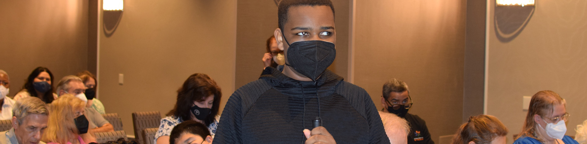 A blind teen stands to speak at a seminar.